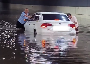 洛阳大雨致司机被困 交警挽起裤子帮忙推车